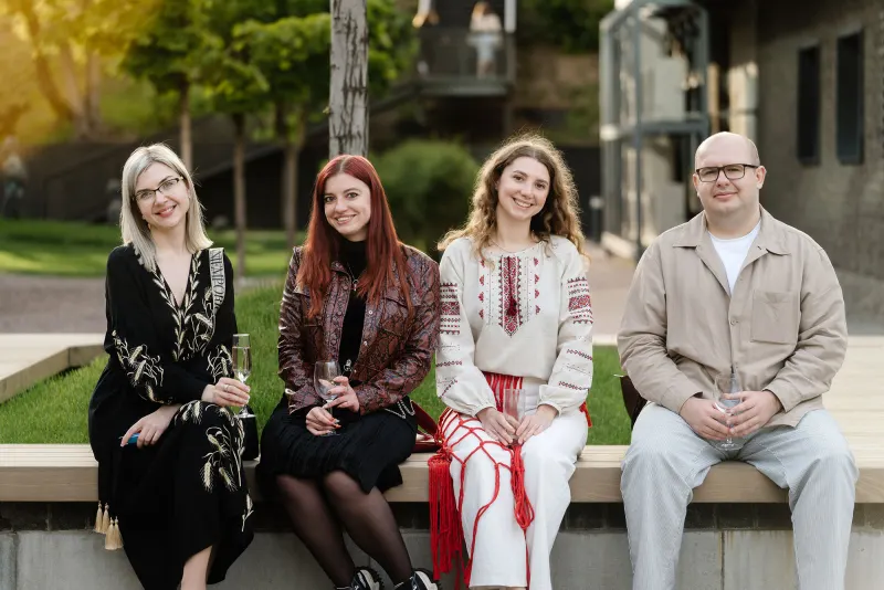 Four people seated on a bench outdoors, two in embroidered shirts, posed together