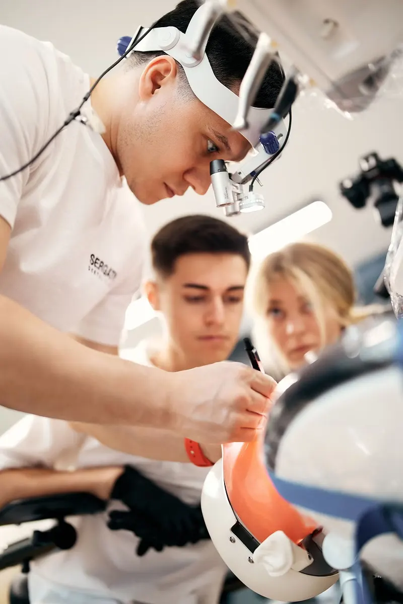 Dentist in a head-mounted loupe demonstrating on a training model as two students watch