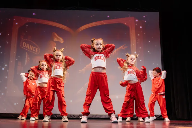 Children's dance troupe posed on stage in red tracksuits under theatre lighting