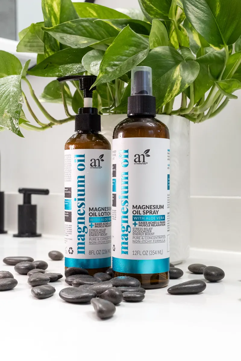 Two bottles of magnesium oil on a white counter with black pebbles and a trailing plant behind