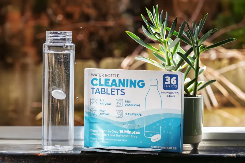 Glass bottle beside a box of cleaning tablets on a windowsill with a plant