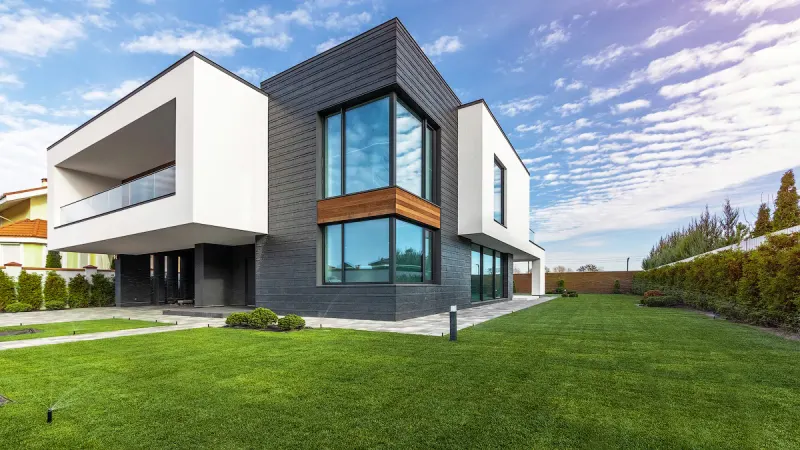 Modern white and grey house with full-height glazing behind a clipped lawn