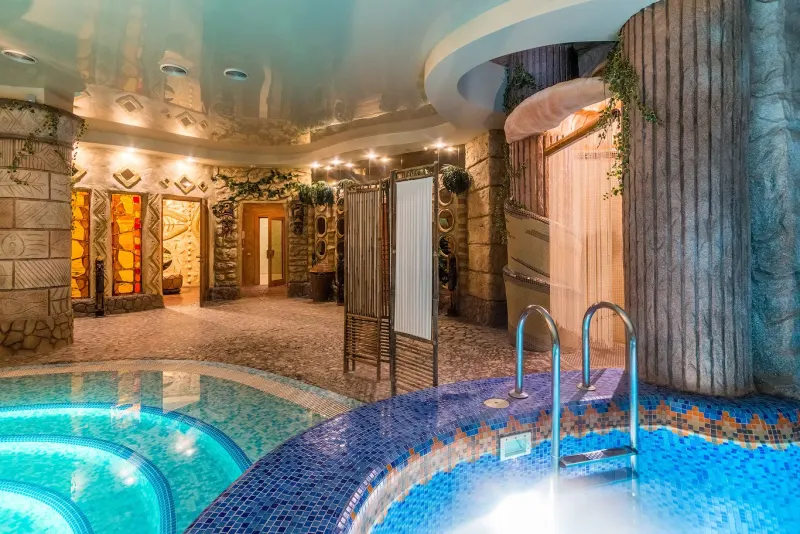 Indoor pool hall with turquoise water, stone columns and warm lighting