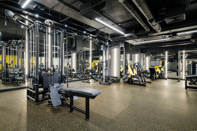 Gym floor with rows of weight machines under an exposed industrial ceiling