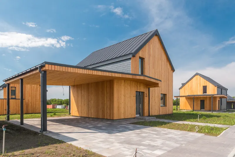 Timber-clad barn-style house with a steep metal roof and gravel drive