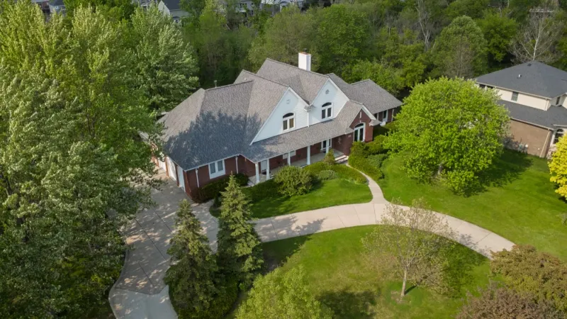 Aerial view of a cream house with a curving drive surrounded by woodland