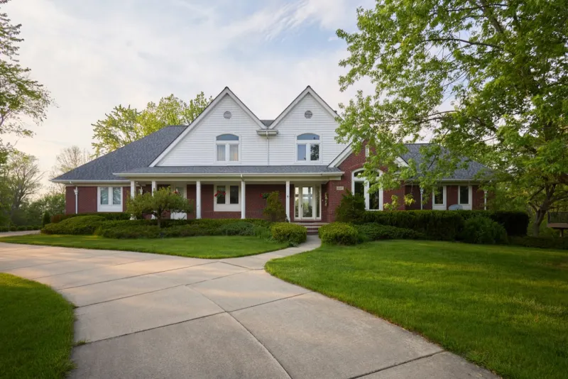 The same home by day, white gables over red brick at the end of a curving drive