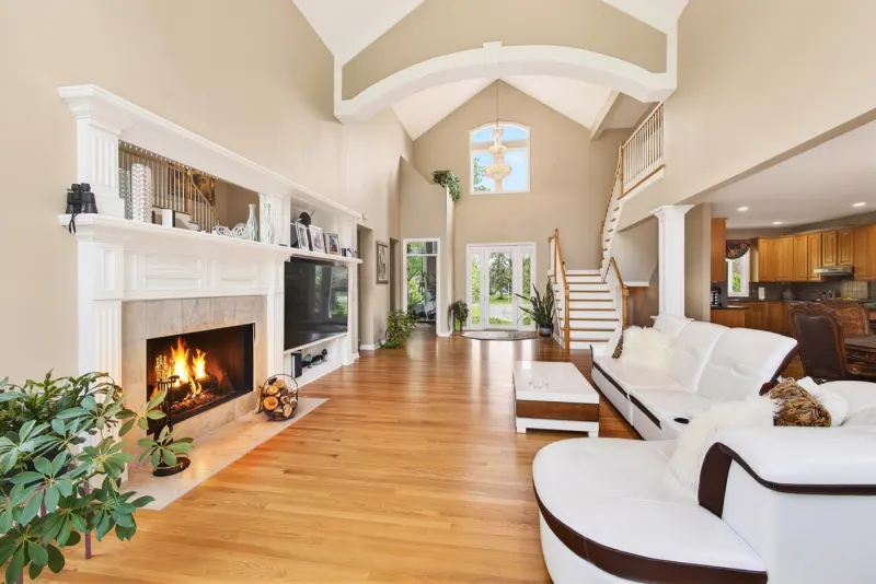 Open-plan living room with a lit fireplace, vaulted ceiling and pale timber floor