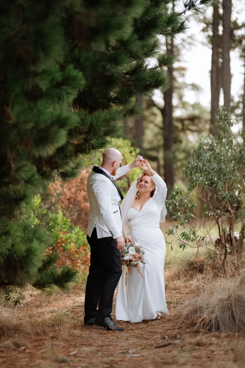 Groom twirling the bride on a pine-needle path beneath tall pines