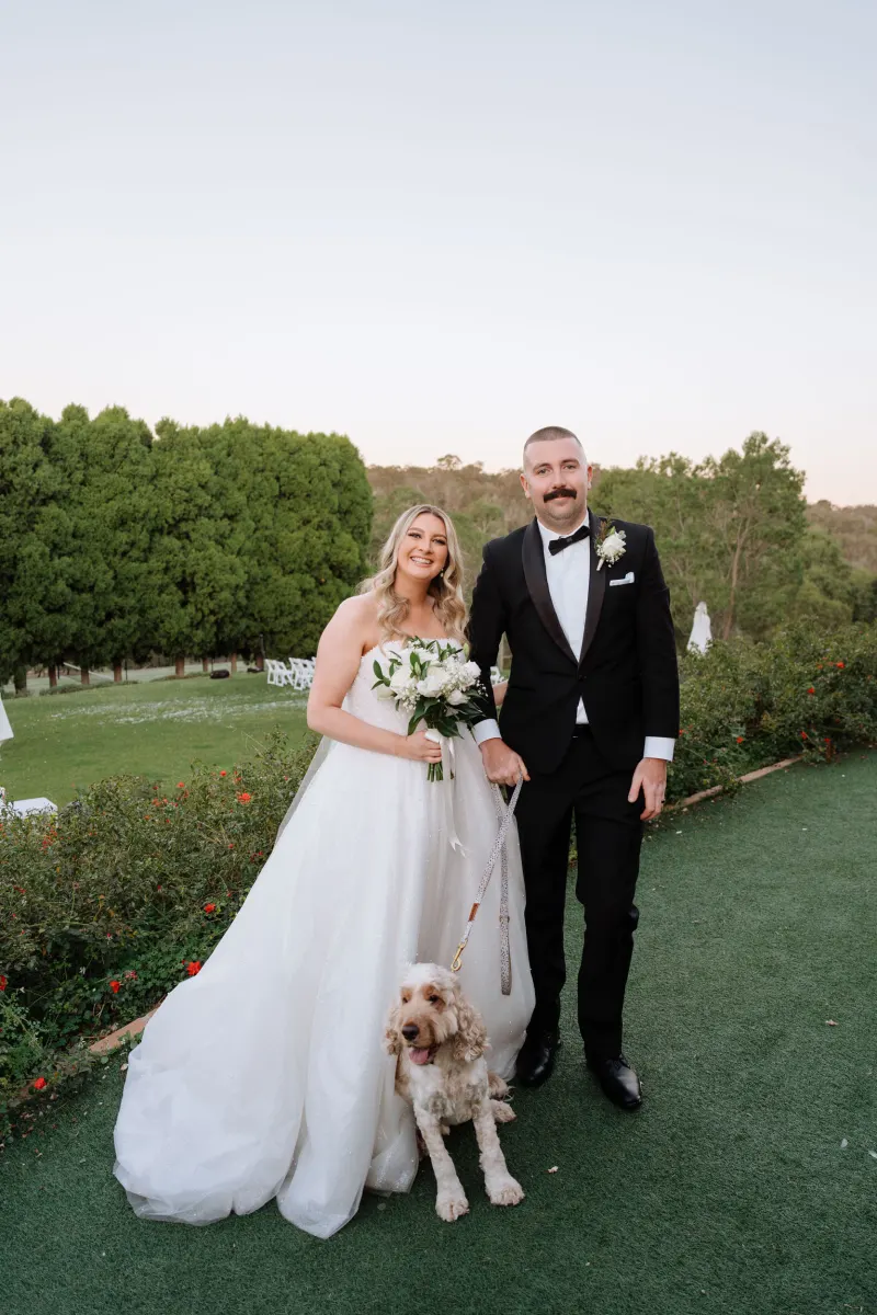 Couple walking across a lawn in low evening light with their curly-haired dog at their feet