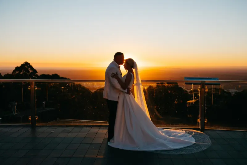 Couple embracing on a hilltop terrace against an orange sunset, the train spread behind