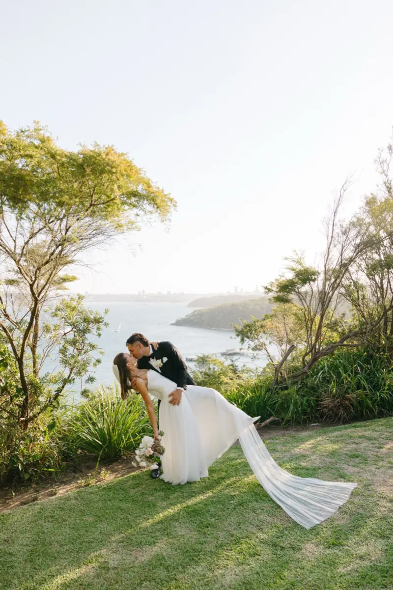 Groom dipping the bride for a kiss on a grassy headland above the coastline